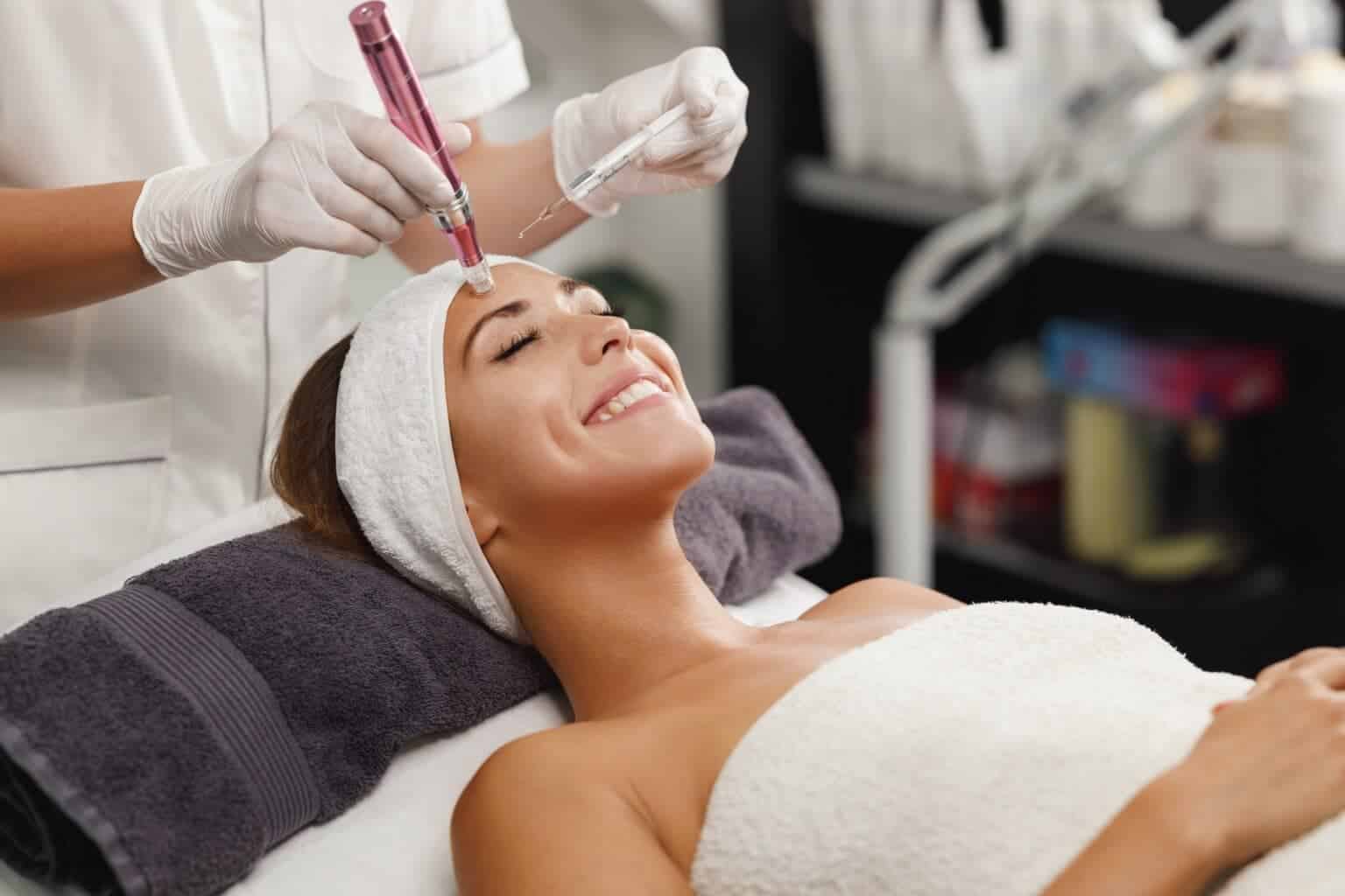 Esthetician performing a microneedling treatment on a smiling client